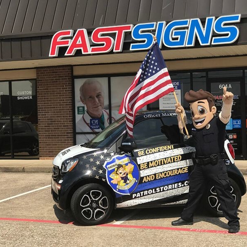 Patrol Stories mascot standing in front of wrapped vehicle at FASTSIGNS of Allen, TX