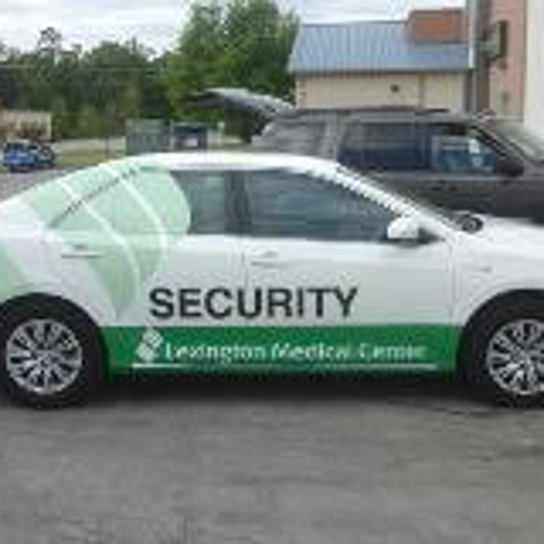 A vehicle with security graphic design parked on a lot with car son the side