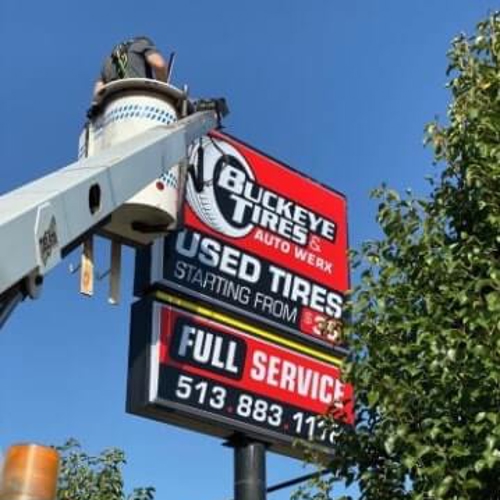 Crane truck carrying a man on top of buckeye tires signage 